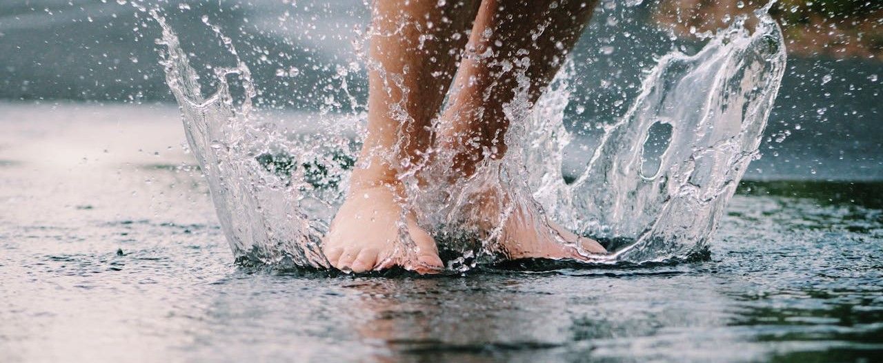 Füße in einer spritzenden Regenpfütze 